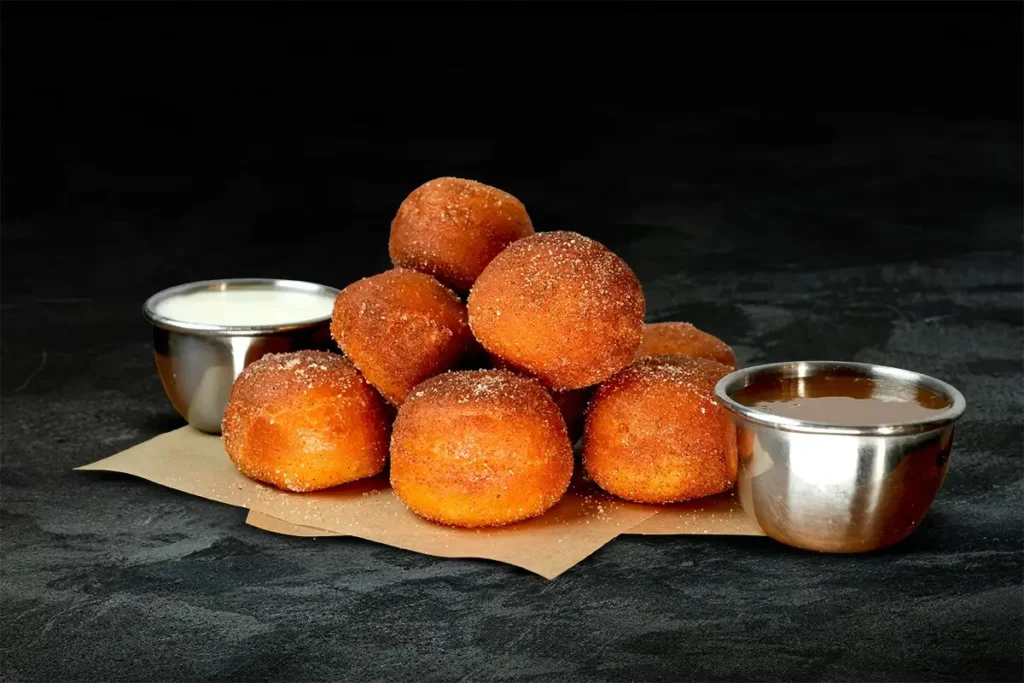 Cinnamon sugar–coated donut bites stacked on parchment paper with two dipping sauces