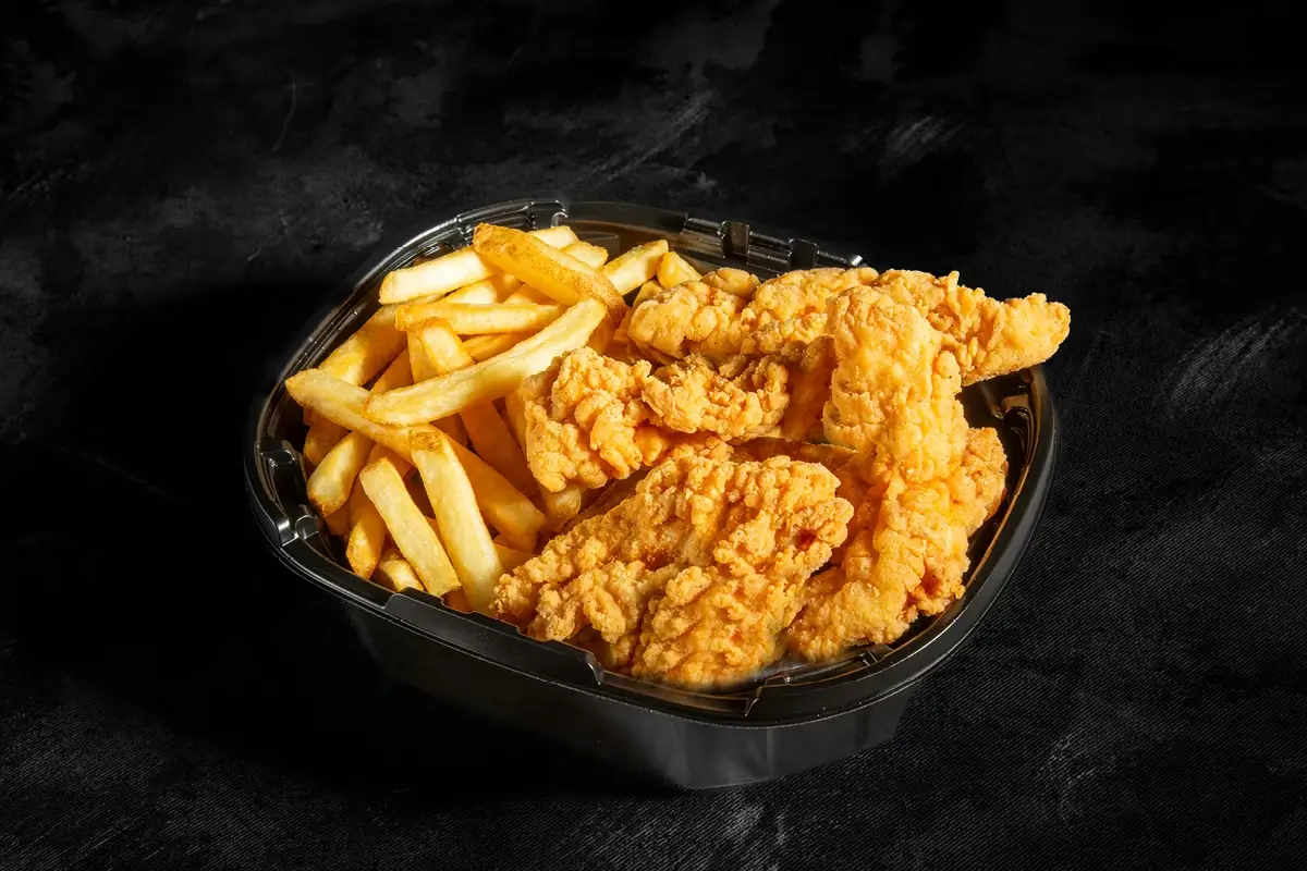 Fried chicken tenders and golden fries in a black takeout container on a dark background