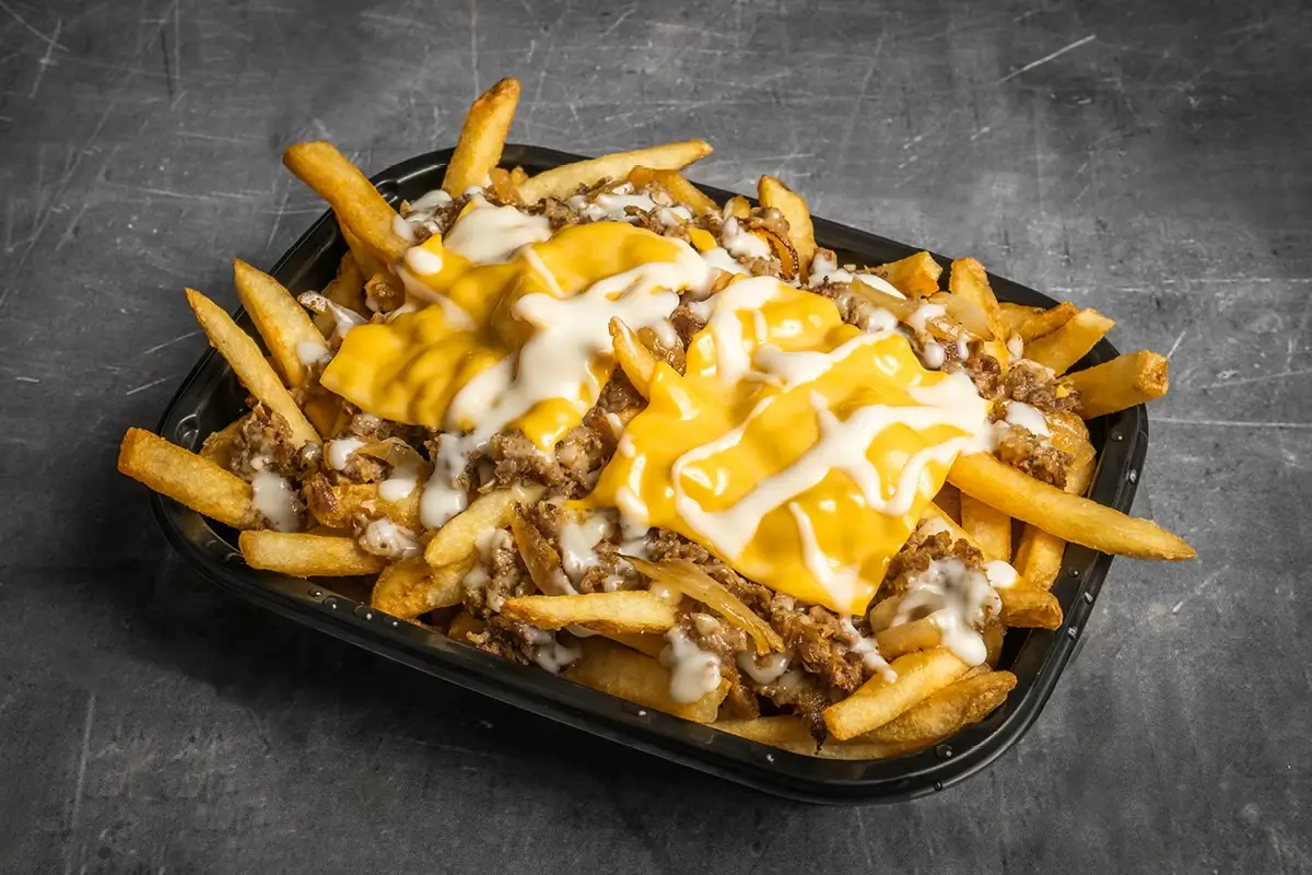 Cheesesteak fries topped with chopped beef, melted cheese sauce, and white sauce in a black takeout container